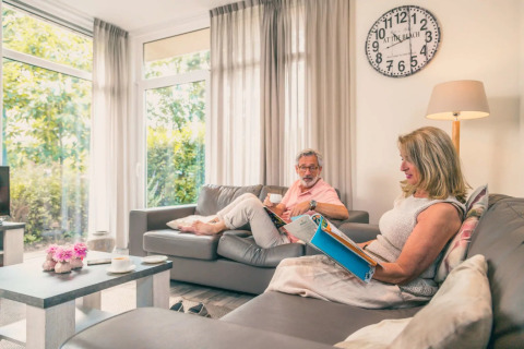 Pareja relajándose en una sala luminosa y moderna con ventanales en un parque de vacaciones glamping.