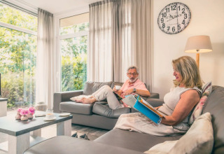 Pareja relajándose en una sala luminosa y moderna con ventanales en un parque de vacaciones glamping.