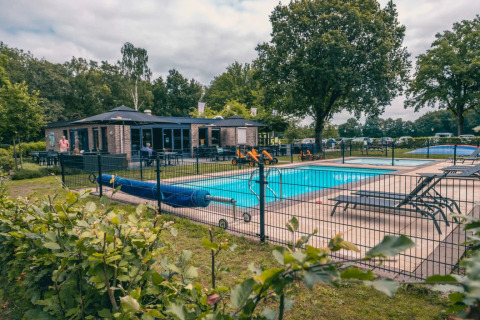 Vakantiepark met glamping, zwembad, ligstoelen, speelgoed en een gebouw in een groene omgeving.