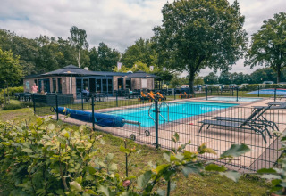 Vakantiepark met glamping, zwembad, ligstoelen, kinderspeelgoed en een gebouw in een groene setting.