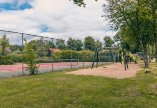 Aire de jeux et court de tennis dans un parc de vacances avec hébergements glamping, entouré d’arbres.