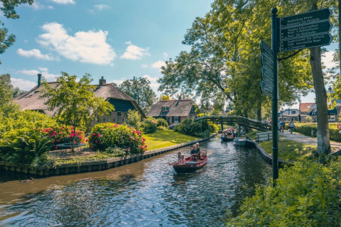 Parque vacacional con glamping, botes en el canal, jardines verdes y pintorescas casas con techo de paja.
