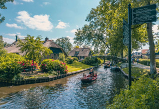 Vakantiepark met glamping, bootjes op een idyllische gracht, bloemenrijke tuinen en rieten huisjes.
