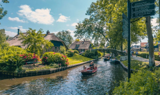 Parque vacacional con glamping, botes en el canal, jardines verdes y pintorescas casas con techo de paja.