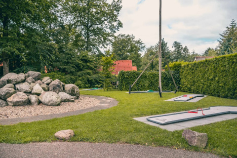 Mini golf course at a holiday park with glamping accommodations, surrounded by greenery and large rocks.