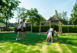 Famille jouant sur une aire de jeux dans un parc de vacances avec hébergements en glamping et verdure.