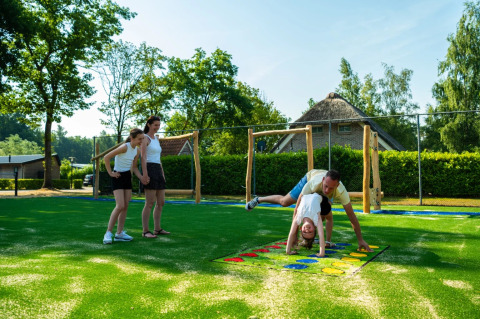 Familie nyder udendørs leg på en legeplads i et feriepark med glampingmuligheder og grønne omgivelser.