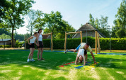 Famille jouant sur une aire de jeux dans un parc de vacances avec hébergements en glamping et verdure.