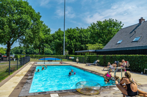 Piscina al aire libre en un parque vacacional con glamping, huéspedes nadando y relajándose bajo el sol.