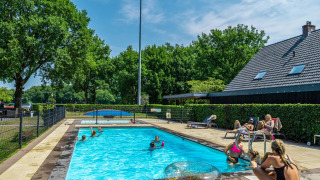 Piscina al aire libre en un parque vacacional con glamping, huéspedes nadando y relajándose bajo el sol.