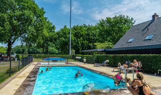 Piscina al aire libre en un parque vacacional con glamping, huéspedes nadando y relajándose bajo el sol.