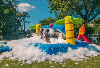 Bambini giocano nella schiuma su un parco giochi gonfiabile con palme in un villaggio vacanze con glamping.