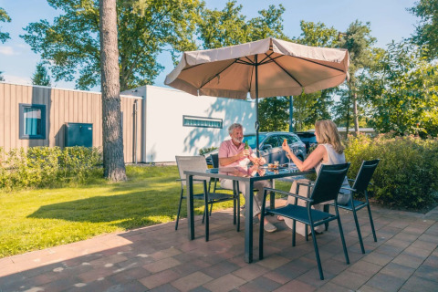Zwei Personen essen draußen an einem Tisch unter einem Sonnenschirm in einem Ferienpark mit Glamping.