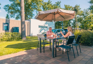 Zwei Personen essen draußen an einem Tisch unter einem Sonnenschirm in einem Ferienpark mit Glamping.