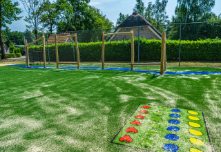 Buitenspeeltuin met kunstgras, klimtoestellen en kleurrijke spellen bij een glamping vakantiepark.