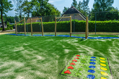 Buitenspeeltuin met kunstgras, klimtoestellen en kleurrijke spellen bij een glamping vakantiepark.