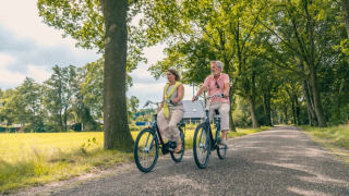 Dos personas pedalean por un camino arbolado en un parque de vacaciones que ofrece alojamiento glamping.