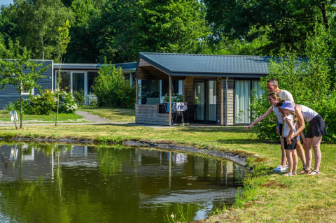 Famille admirant un étang devant des cabanes modernes dans un parc de vacances glamping tout confort.