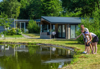 Famille admirant un étang devant des cabanes modernes dans un parc de vacances glamping tout confort.
