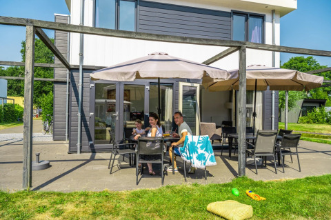 Familia descansando bajo sombrillas en la terraza de una casa glamping moderna en un parque vacacional.