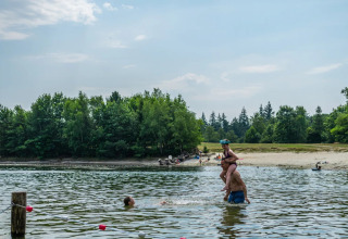 Mensen zwemmen in een meer bij een strand in een vakantiepark met glamping accommodaties.