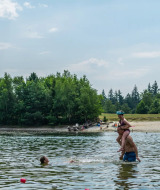 Personas nadando y jugando en un lago junto a una playa en un parque vacacional con glamping.