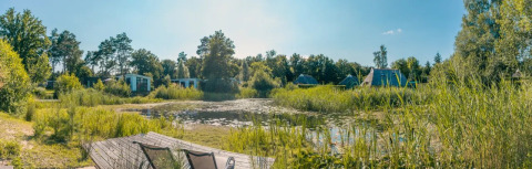 Vista panorámica de cabañas glamping junto a un estanque en un parque de vacaciones con vegetación.