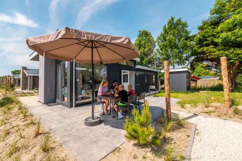 Family relaxing and dining outdoors under a large umbrella at a modern glamping holiday park.