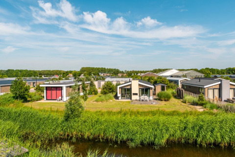 Foto van moderne glamping-accommodaties in een vakantiepark met gras, bomen en blauwe lucht.