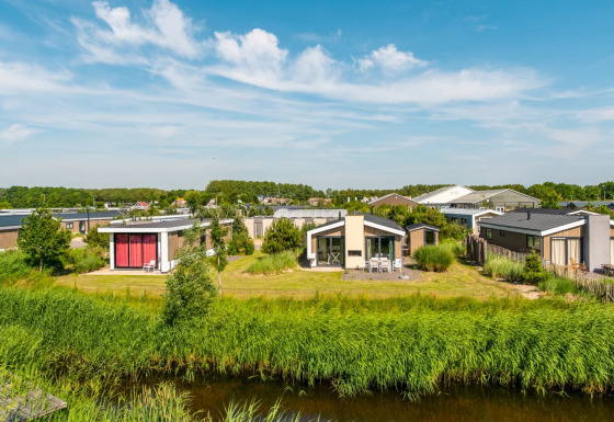 Foto af moderne glamping-hytter i et feriepark med grønt græs og blå himmel på en solrig dag.