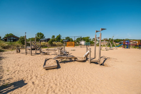Spielplatz mit Sandboden in einem Ferienpark mit Glamping-Unterkünften und blauem Himmel.