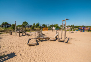 Legeplads med sandbund ved et ferieområde med moderne glamping-hytter og klar blå himmel.