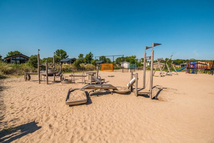 Aire de jeux sur sable dans un parc de vacances avec hébergements glamping et ciel bleu dégagé.