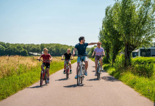 Gezin fietst samen op een zonnige dag langs bomen en grasvelden bij een vakantiepark met glamping.