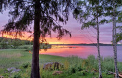 Solnedgang over søen ved Camping Falkudden i Dalarna, Sverige, med træer i forgrunden og farverige skyer.