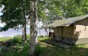 Safari tent by the lakeside, nestled among green trees on a sunny day, perfect for a nature getaway.