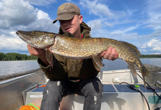 Un giovane seduto in barca a Camping Falkudden, Dalarna, Svezia, tiene in mano un grande luccio appena pescato.