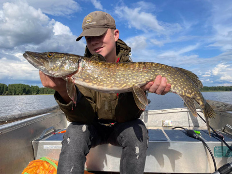 Een jongere zit in een boot op Camping Falkudden, Dalarna, Zweden, met een grote vers gevangen snoek.