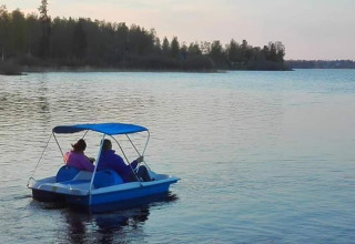 Two people ride a pedal boat on a calm lake at Camping Falkudden, surrounded by trees in Dalarna, Sweden.
