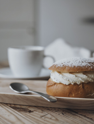 Semla sueca con nata y azúcar glas sobre bandeja de madera, junto a un café en By Kyrkby, Dalarna.