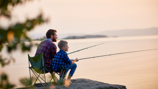 Father and son are fishing together on a waterfront rock
