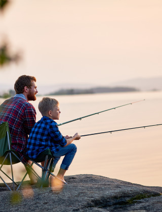 Father and son are fishing together on a waterfront rock