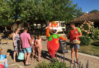 Familier hygger sig med en maskot og personale på Le Camp de Florence feriepark i Occitanie, Frankrig.