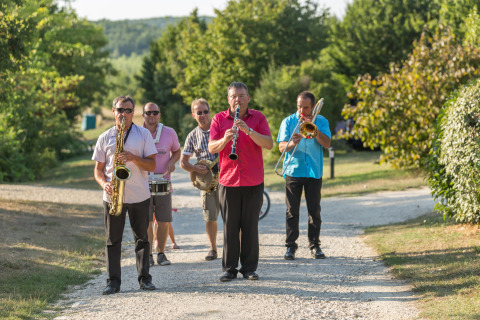 Cinq musiciens jouent de leurs instruments sur un chemin, au Camp de Florence, parc de vacances en Occitanie.