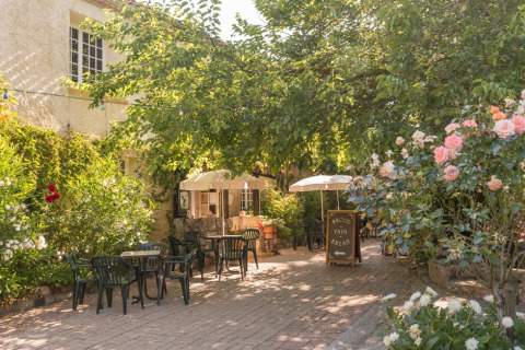 Outdoor terrace with tables, chairs, parasols and flowers at a holiday park in Occitanie, France.