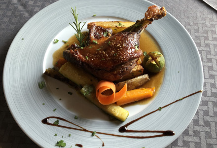 Plato elegante de confit de pato con verduras asadas y hierbas, servido cerca de La Romieu, Occitania, Francia.