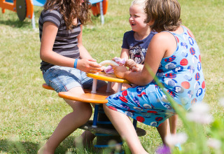 Drei Kinder spielen lachend auf einem Spielplatz im Ferienpark Camp de Florence in Occitanie, Frankreich.