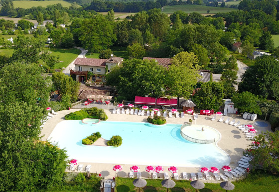 Vista aerea della piscina e del parco vacanze Le Camp de Florence in Occitania, Francia, immerso nel verde.