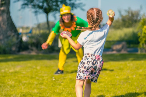 Kind met waterballonnen gooit naar verklede entertainer in een vakantiepark met glamping accommodaties.