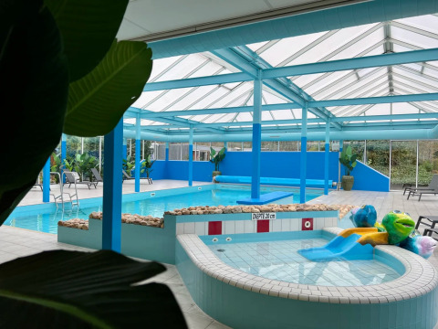 Overdekt zwembad met kinderbad, glijbaan en ligstoelen bij een vakantiepark dat glamping aanbiedt.